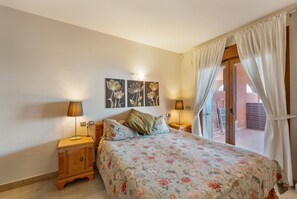 Ein Schlafzimmer mit einem Bett, zwei Nachttischen mit Lampen, einer Wandleuchte und einer Glastür zum Außenbereich.