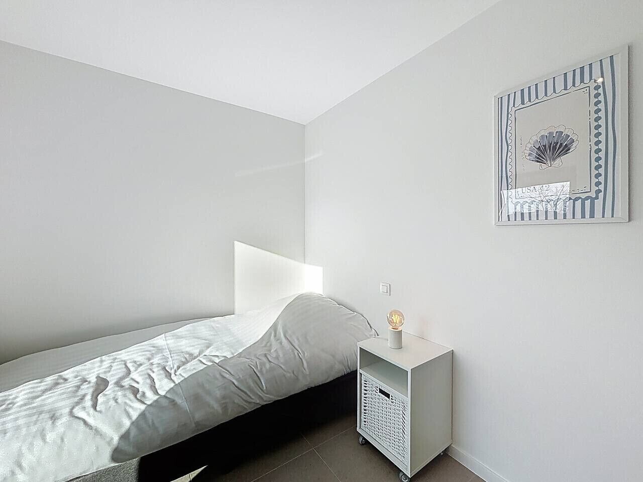 A minimalist bedroom with a bed, a nightstand, and a wall-mounted light fixture.