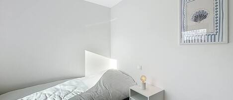 A minimalist bedroom with a bed, a nightstand, and a wall-mounted light fixture.