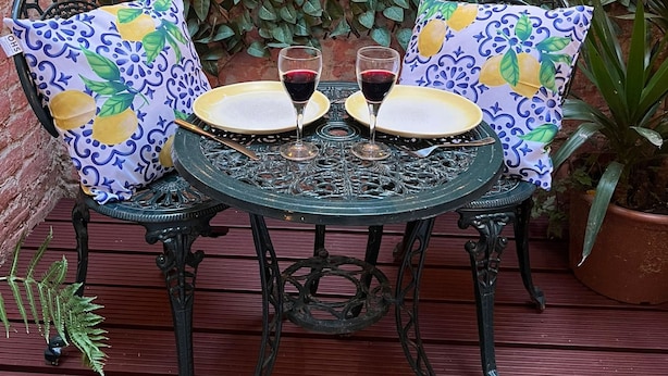 A table set with two wine glasses and plates, surrounded by chairs with patterned cushions, against a wall of green foliage and string lights. - Chelsea 2BR Private Courtyard Earl s Court Tube (London)