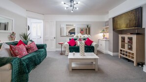 A living room with a green sofa, a white coffee table, and a TV on the wall. - Chelsea 2BR Private Courtyard Earl s Court Tube (London)
