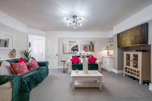 A living room with a green sofa, a white coffee table, and a TV on the wall. - Chelsea 2BR Private Courtyard Earl s Court Tube (London)