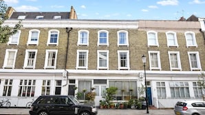 A row of terraced houses with white-framed windows, a black car parked on the street, and a bicycle leaning against the wall. - Chelsea 2BR Private Courtyard Earl s Court Tube (London)