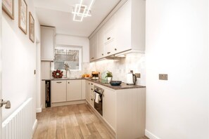 A kitchen with white cabinets, a window, and a radiator. - Kensington Chelsea 1BR Patio Apartment Tube (London)