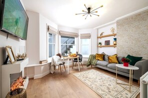 A living room with a fireplace, a television, a sofa, a coffee table, and a patterned rug. - Kensington Chelsea 1BR Patio Apartment Tube (London)