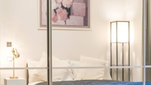 Un dormitorio con cama, almohadas, una mesita de noche, una lámpara y una obra de arte enmarcada en la pared.