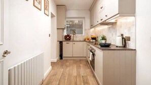 Cocina estrecha con armarios blancos, suelo de madera y ventana decorada con un adorno.