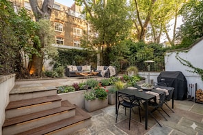 A patio with a table and chairs, a sofa, and a grill. - Kensington Chelsea 2BR Garden Apartment Tube (London)