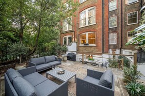 A patio with outdoor furniture, a barbecue grill, and a view of a brick building. - Kensington Chelsea 2BR Garden Apartment Tube (London)