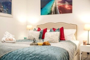 A neatly made bed with a blue quilt, white pillows, and a red pillow. There is a tray with a croissant and orange juice on the bed. - Chelsea 5BR Family Home Walk to Earl s Court Tube (London)