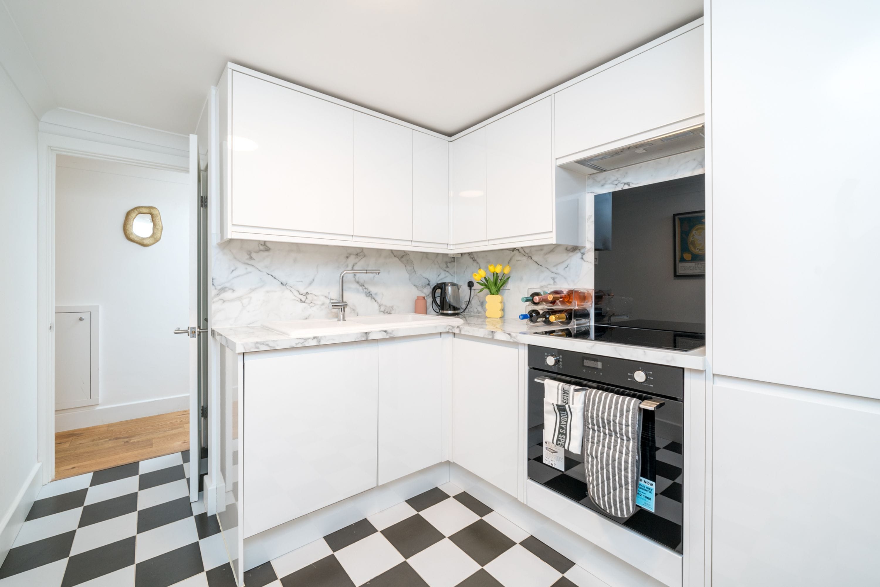 A modern kitchen with white cabinets, a marble countertop, a black oven, and a checkered floor.