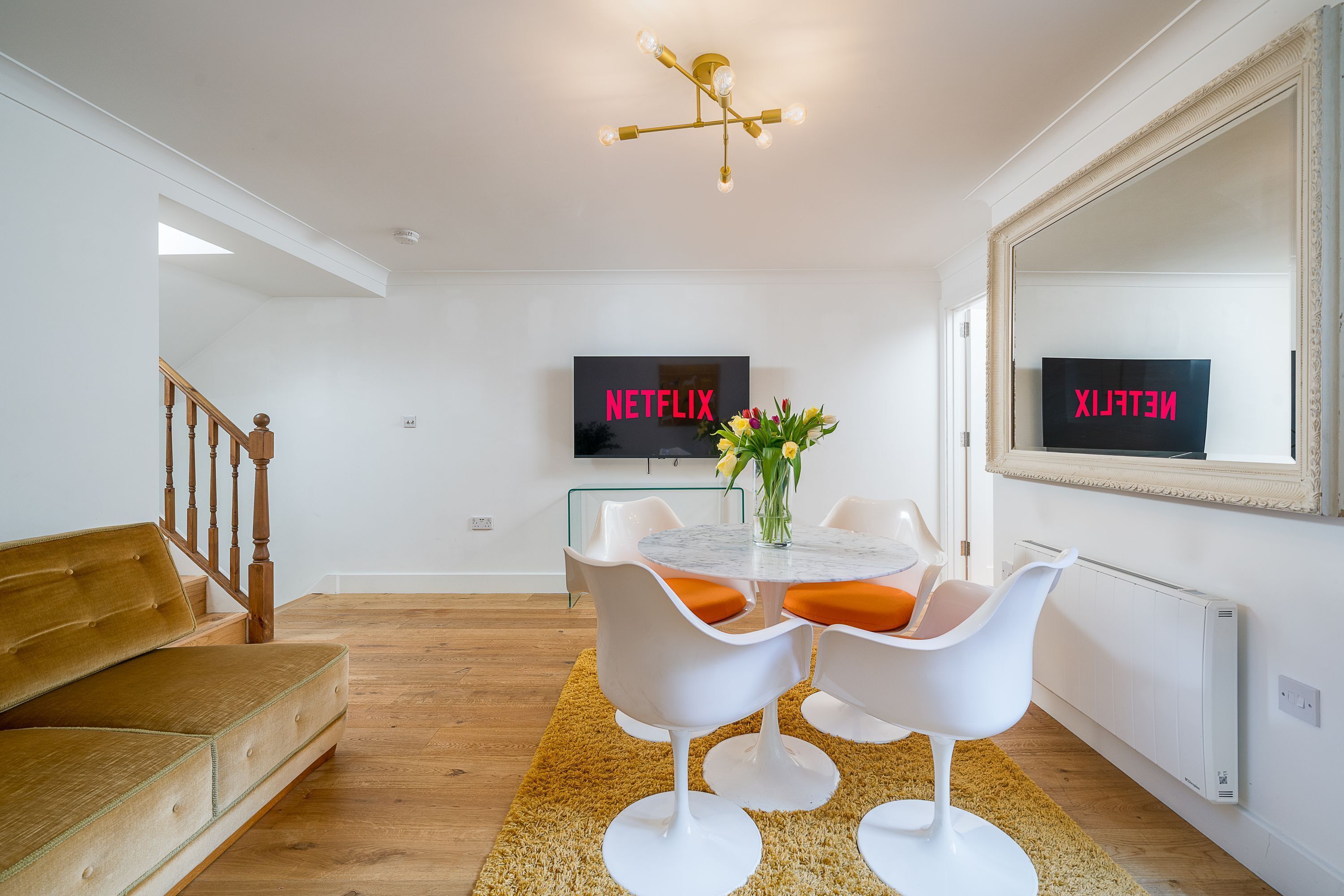 A modern living room with a sofa, a dining table with chairs, a TV, and a large mirror.