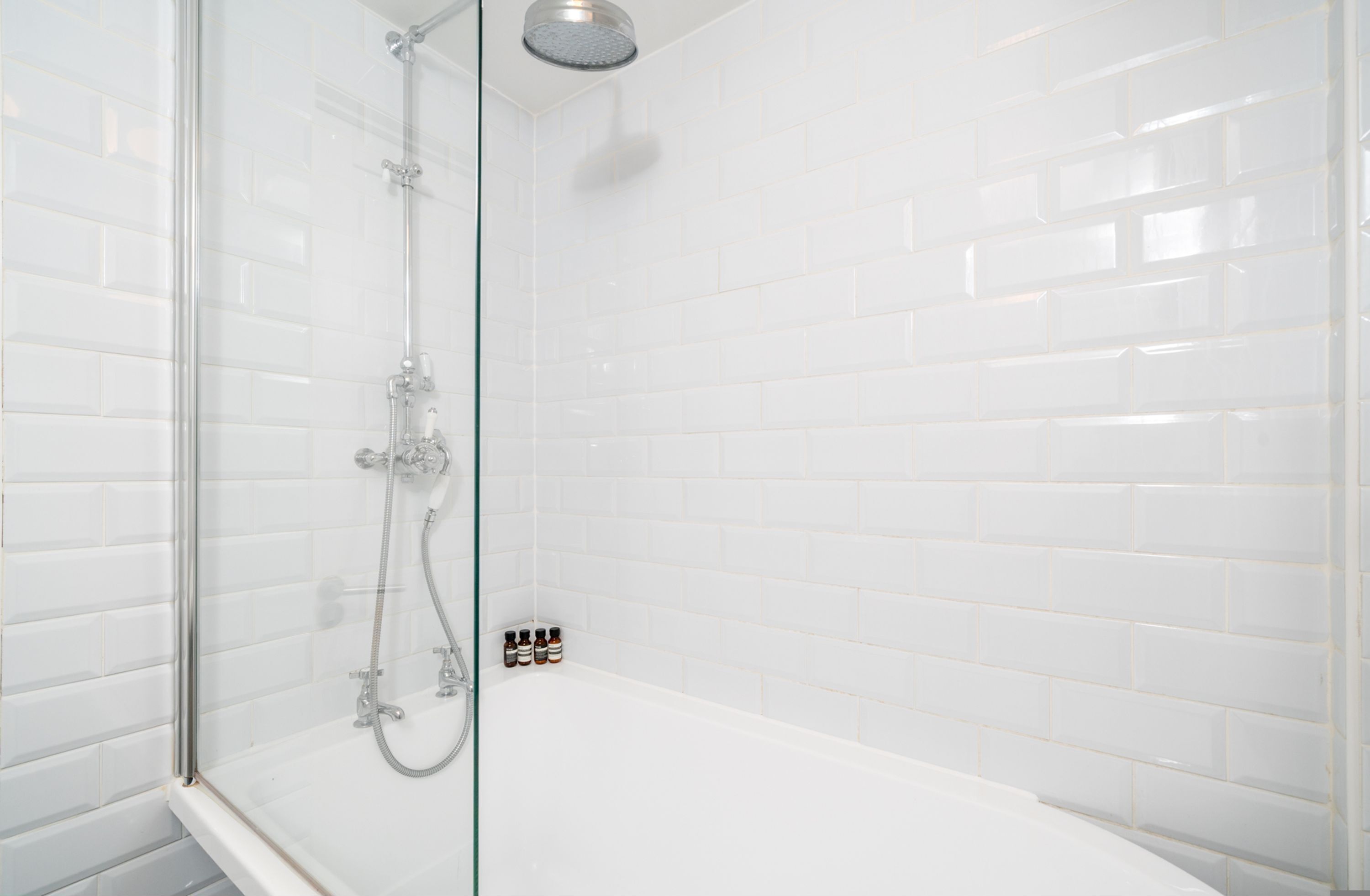 A glass-enclosed shower with white tiled walls and a white bathtub.
