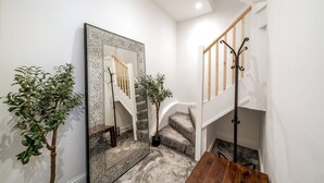 A staircase with a wooden handrail and a metal banister, a large mirror with a decorative frame, and two potted plants. - Earl s Court Chelsea 4BR Duplex Ap Walk to Tube (London)