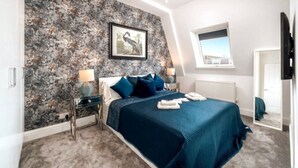 A bedroom with a bed, a nightstand, a lamp, a framed picture on the wall, a window, and a door. - Earl s Court Chelsea 4BR Duplex Ap Walk to Tube (London)