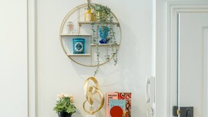 A wall-mounted shelf with decorative items, a potted plant, and a book titled 'SALADS ARE INDIA.' - Earl s Court Chelsea 1BR Elegant Stay Tube (London)