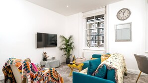 A living room with a flat-screen TV, a potted plant, a sofa, and a table with a bottle. - Earl s Court Chelsea 1BR Elegant Stay Tube (London)