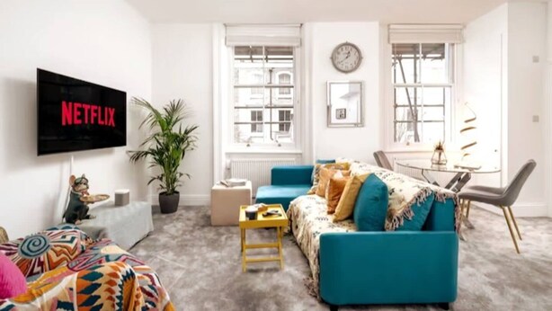 A modern living room with a flat-screen TV, a sofa, a coffee table, and a dining area with a table and chairs. - Earl s Court Chelsea 1BR Elegant Stay Tube (London)
