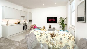 A modern living space with a kitchen, dining area, and a flat-screen TV mounted on the wall. - Earl s Court Chelsea 1BR Elegant Stay Tube (London)