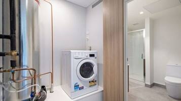 A compact bathroom with a washing machine, a glass shower enclosure, and a toilet.