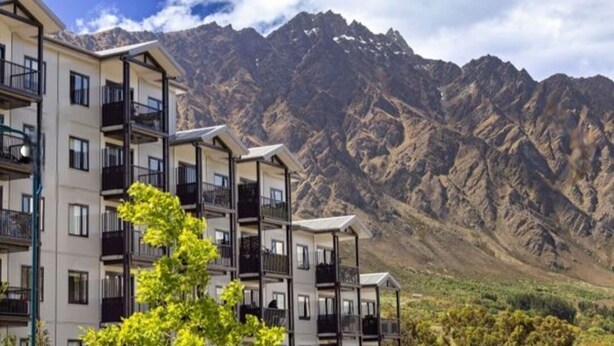 A multi-story hotel with balconies, set against a mountainous backdrop. - Mountain View Exchange (Queenstown)
