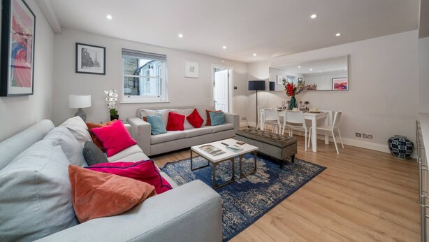 A modern living room with a grey sofa, a coffee table, and a dining area with a white table and chairs. - Earl s Court Chelsea 2BR Modern Apt Walk to Tube (London)