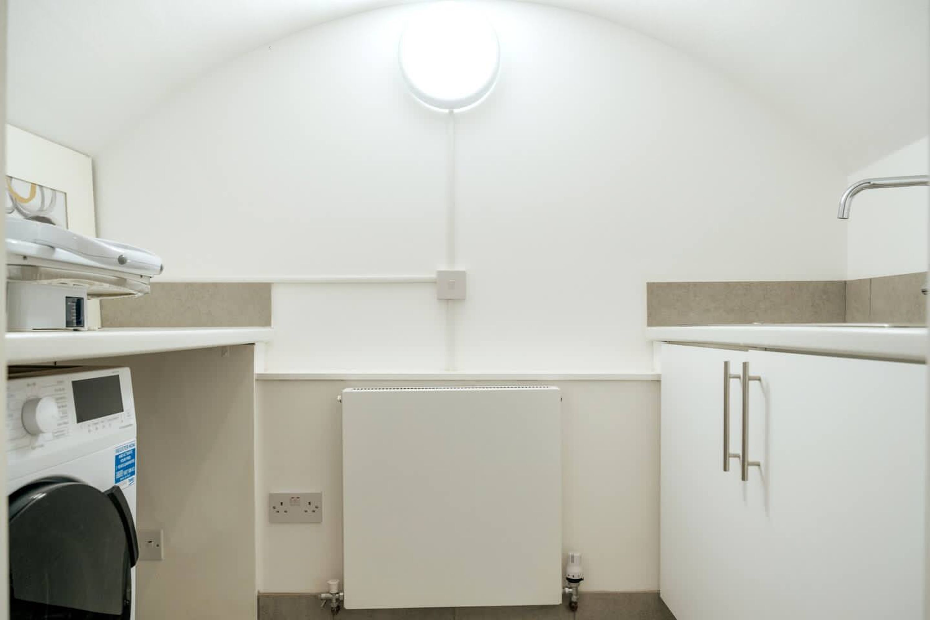 Une petite salle de bain équipée d’un lave-linge encastré, d’un radiateur et d’un meuble de rangement.