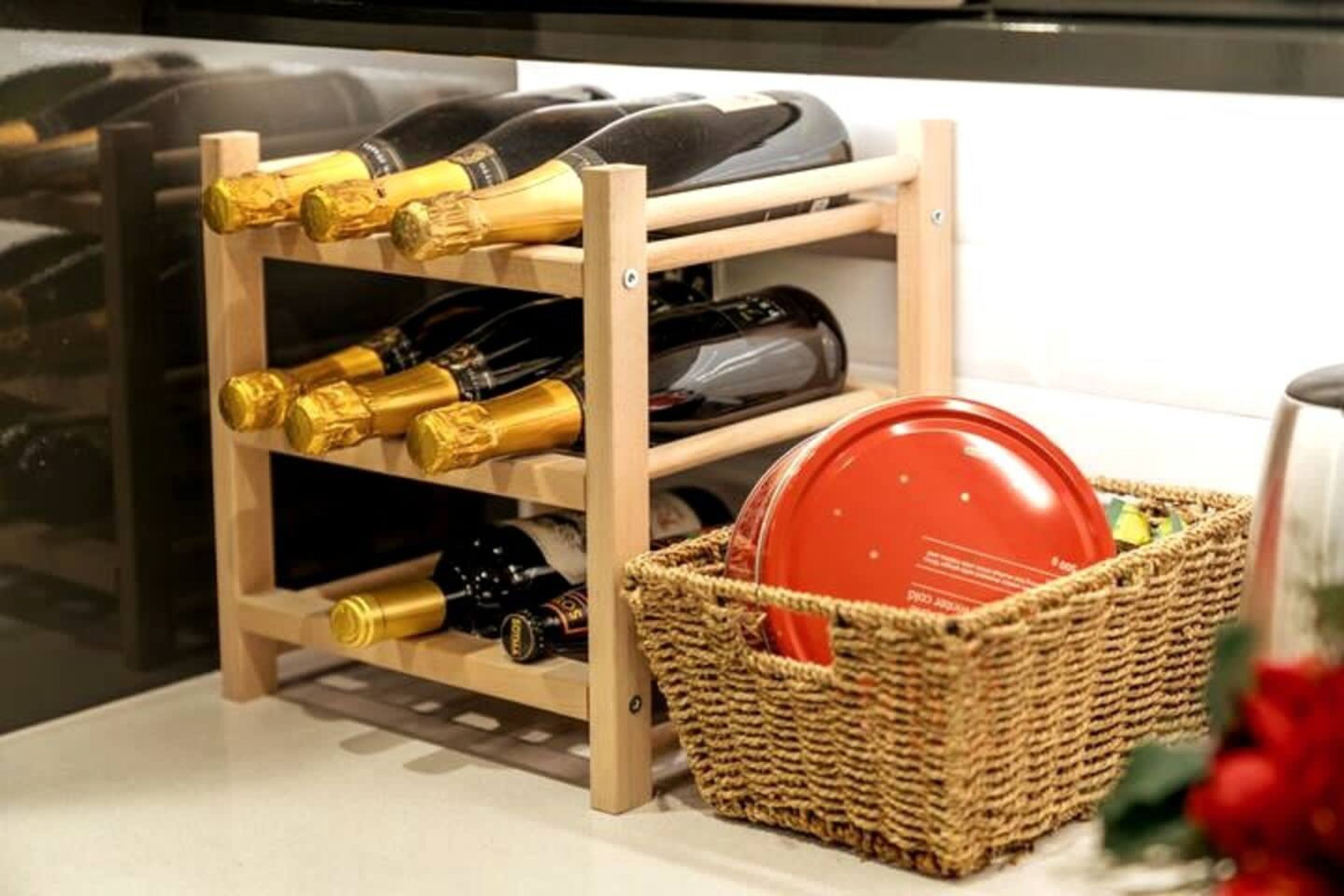 Een houten wijnrek met flessen en een mandje met een rode schaal.
