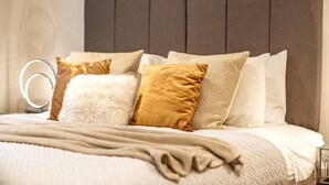 Ein Bett mit Kopfteil, mehreren Kissen, einer Decke und einem Nachttisch mit Spiegel.