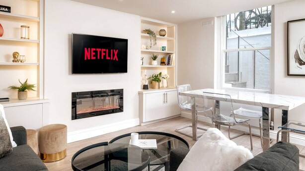 Ein modernes Wohnzimmer mit Kamin, Essbereich und einem Fernseher, der 'NETFLIX' anzeigt.