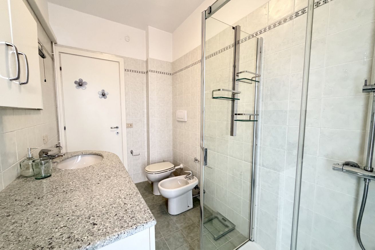 A bathroom with a granite countertop, a sink, a toilet, a bidet, and a glass-enclosed shower.