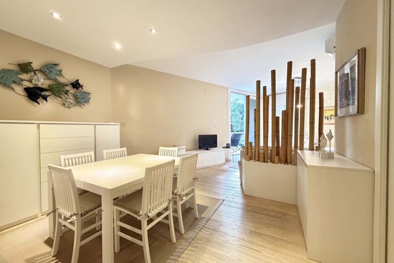Un espace repas moderne avec une table et des chaises blanches, un élément décoratif mural et une sculpture en bambou.