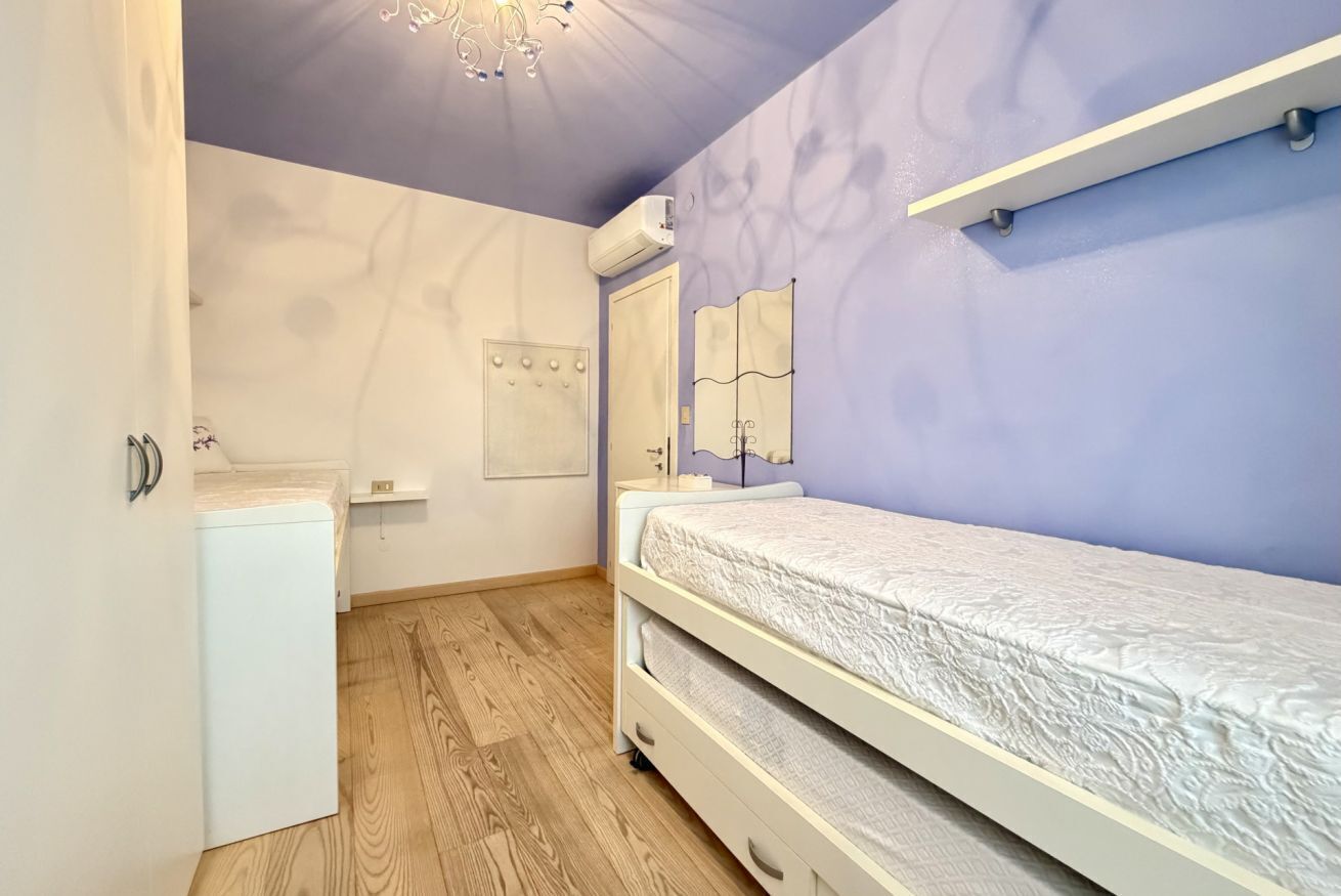 A bedroom with a bed, a small white cabinet, a mirror, and a ceiling light fixture.