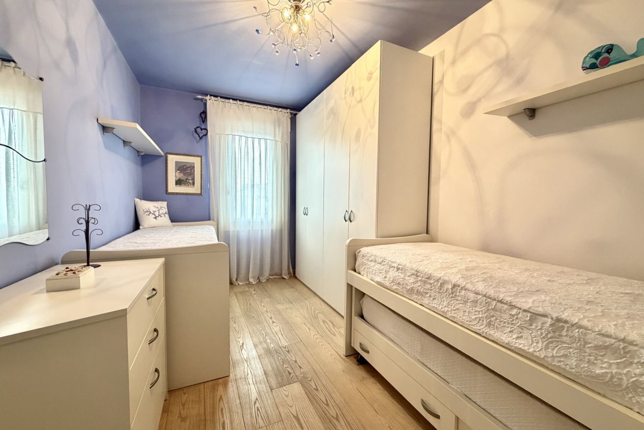 A bedroom with a bed, a desk, a wardrobe, and a chandelier.