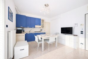 Eine moderne Küche mit blauen Schränken, einem Esstisch mit Stühlen, einem weißen Kühlschrank und einem Fernseher.