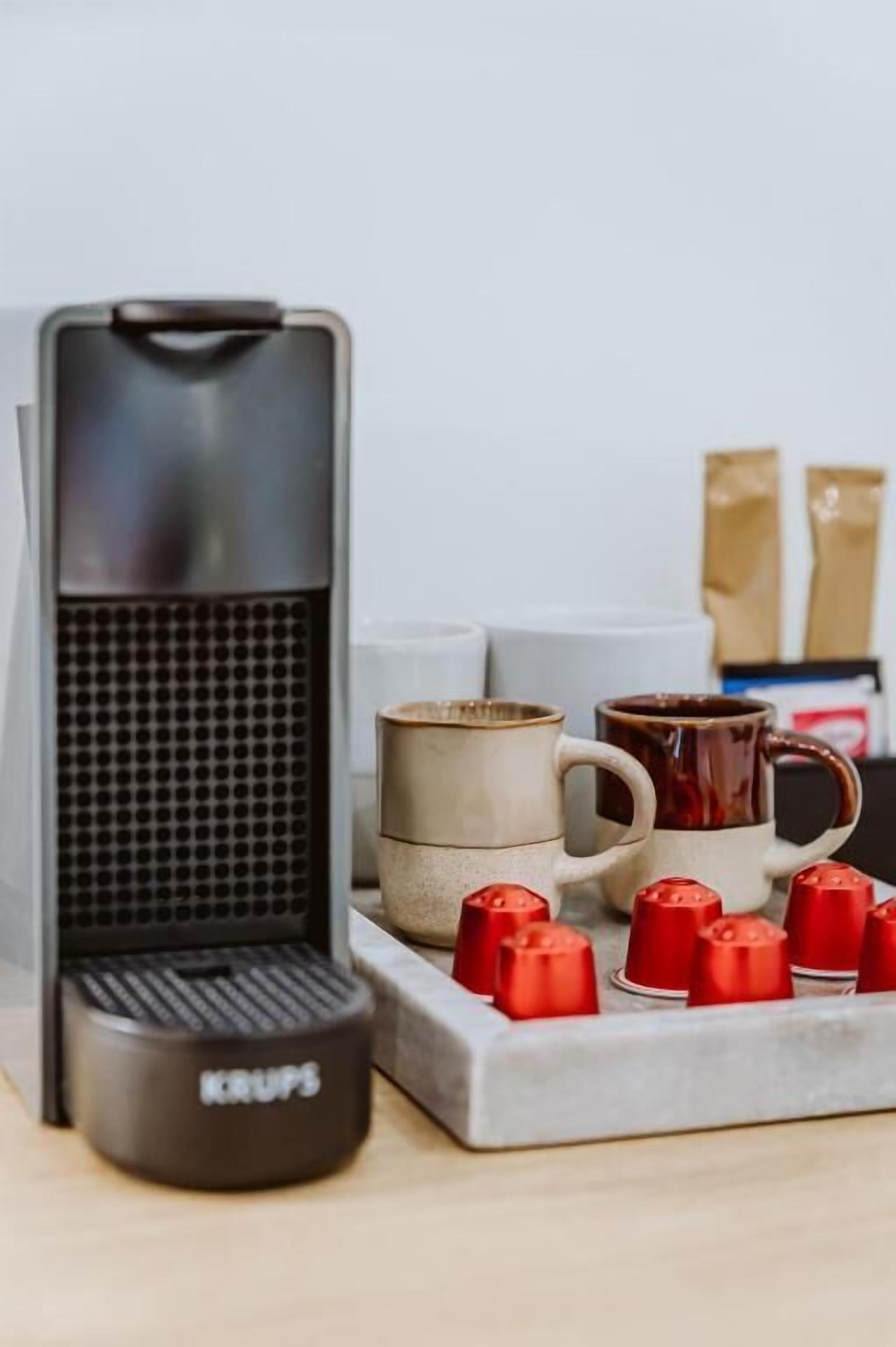 A coffee maker with a Krups brand, a stack of mugs, and a coffee grinder on a countertop.