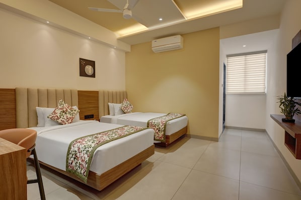 A hotel room with two beds, a ceiling fan, an air conditioning unit, a TV, and a plant.