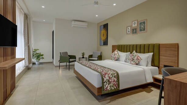 Ein Hotelzimmer mit Bett, Schreibtisch, zwei Stühlen, Fernseher, Klimaanlage und Deckenventilator.