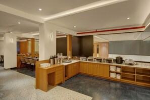 A modern kitchen with a long counter, built-in appliances, and a dining area with chairs. - Rajpath Beacon Hotel Belagavi  (Belagavi)