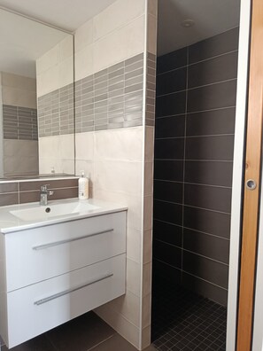 Un baño con lavamanos blanco, espejo y zona de ducha con azulejos oscuros.