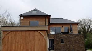 Ein zweistöckiges Haus mit Holztür zur Garage, einer Steinfassade und einem kleinen Balkon mit Sitzbank.