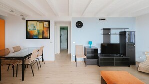 Una sala de estar moderna con una mesa de comedor de vidrio, sillas, un televisor y un cuadro abstracto de gran tamaño.