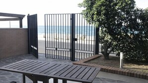 Un patio al aire libre con una mesa y sillas, una verja que da a una playa y un árbol.