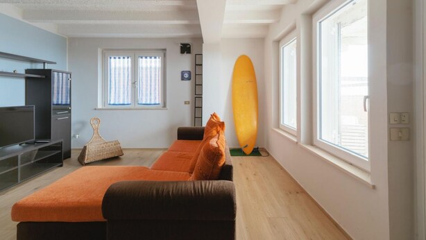 Una sala de estar con un sofá, televisión, ventana y una tabla de surf.