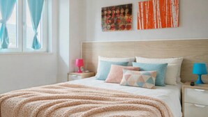 Un dormitorio con una cama, almohadas, una mesita de noche, una lámpara y obras de arte en la pared.