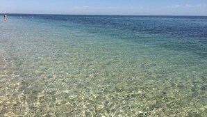 Una vista despejada de una playa con aguas poco profundas, una persona a lo lejos y un cielo claro.