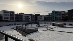Et moderne byområde med flere lejlighedskomplekser, et overdækket udendørs område med snedækket jord, og en mobilkran i baggrunden.