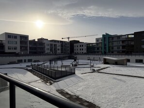A modern building complex with multiple apartment buildings, a covered outdoor area with a snow-covered ground, and a construction crane in the background. - Modern apartment downtown Reykjavik (Reykjavík)