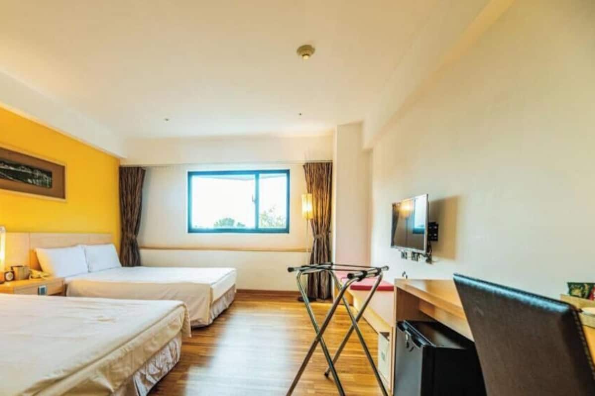 A hotel room with two beds, a window, a television, and a desk with a chair.