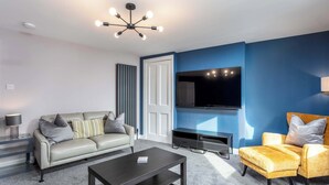 Un salon moderne comprenant un canapé, un fauteuil, une table basse, un téléviseur et un luminaire suspendu au plafond.